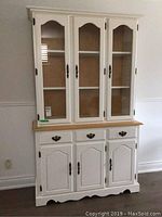 Full front view of white painted china cabinet with detachable hutch, showing glass doors on the upper section and solid paneled doors and drawers below.
