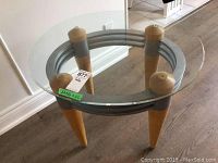 Front angle view of the oval glass top table showing the wooden legs and circular frame supporting the glass.