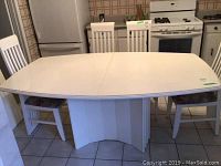 Front view of large white wooden dining table with chairs around it in kitchen setting.