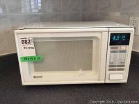 Front view of white Samsung microwave oven on countertop with control panel and digital display visible.