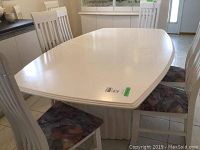 White painted wooden dining table, modern pedestal style, shown with chairs and two leaves visible.
