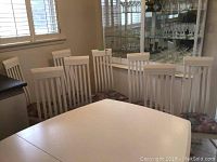Photo showing all eight white painted wood dining chairs arranged behind a dining table, highlighting their modern slatted backs and floral cushioned seats.