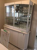 Front view of white painted wood china cabinet with glass doors containing glassware