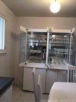 Glass cabinet with shelves displaying assorted glassware and stemware including wine glasses, martini glasses, and water glasses.