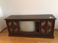 Front view of the vintage wooden TV and stereo cabinet showing the Philco TV and side speaker compartments with carved wood and fabric covering.