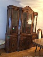 Front angled view of the large ornate wooden china cabinet with carved details, brass pulls, and glass hutch.
