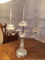 Front and slightly elevated view of the glass candelabra with three lights, crystal fobs, and candles on a wooden table.