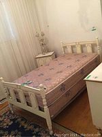 White twin bed set up with mattress and box spring in a bedroom, showing general view of bed and mattress.