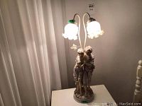Front view of young lovers statue lamp with two lit frosted glass lampshades on curved stems.