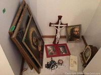Overview of entire lot showing four framed pictures leaning against wall and floor, wooden crucifix, small oratory, and rosaries scattered below