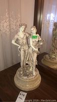 Front and left side view of porcelain statue of young couple on marble base, showing detailed features and condition.