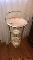 Photo of gold-tone metal wash basin stand with round pink and white ceramic basin, ceramic water pitcher, and separate ceramic soap dish