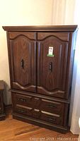 Front view of wood armoire with double doors and two drawers at bottom.