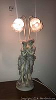 Front view of statue lamp showing the young lovers' statue base and the two illuminated flower-shaped glass lamp shades.