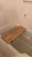 Wooden shower seat placed over a bathtub with tiled walls.