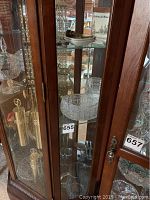 Glass cabinet showing clear cut glass bowl, pitcher, and mugs along with other glassware items
