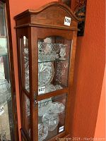 Front view of brown wooden display shelf with tempered glass door and side panels, showing arched top.