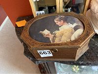 View of the octagonal wooden jewelry box with painted lid showing a woman reading a book, carved detail on edges, and keyhole on front.