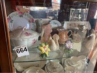 Glass cabinet shelf showing Warren silver plated sugar bowl, salt and pepper shakers, ceramic flowers and animal figures, and china plates with pink rose pattern.