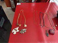 Lot items arranged on red table showing heart pendants, brooches, angel pins, chains, and necklaces.