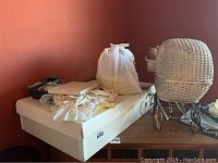 Vintage baby carriage on top of wooden cabinet with stack of vintage baby clothes and fabric bundles on white box.