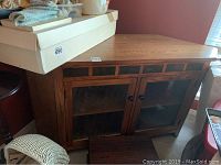 Full view of wood corner cabinet showing front left corner with two glass paneled doors and two small drawers above.