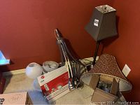 Metal chandelier, lamp shades, and table lamp grouped on floor against orange wall