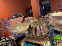 View of tortilla serving dish with floral pastel design and several shiny tin cake pans on rack.