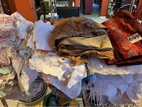 Pile of assorted white, cream, pastel lace and embroidered tablecloths stacked on a table.
