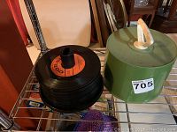Stack of black vinyl records with orange Coral label placed vertically on a metal rack beside a green cylindrical record holder with a cream handle on top.
