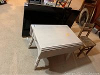 White drop leaf side table seen at an angle with closed leaves and visible wear and age marks