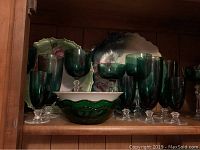 Green glass stemware including goblets and wine glasses, matching green glass bowl, and two green ceramic plates with floral accents in background