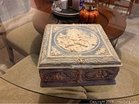 Square jewelry box with detailed carved lid and sides placed on glass table