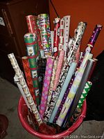 Multiple rolls of holiday-themed Christmas wrapping paper placed upright in a container