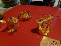 Three gold-tone Christmas ornaments including a clock house and sleigh on a red tablecloth.