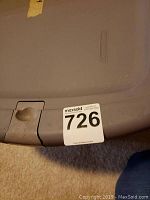 Plastic storage container lid with auction lot tag number 726 attached, used to hold the ornaments.