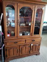 Frontal photo of the vintage Early American hutch showing three glass doors above and wooden cabinet doors below with drawers in the middle.