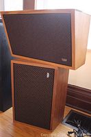 Photo of two McCurdy LSA609 amplified studio monitor speakers stacked, showing angled upper speaker cabinet and fabric grill with logo.