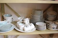 Shelf display of Wedgwood pale green glazed bowls and plates alongside stacks of Royal Copenhagen “Quaking Grass” pieces