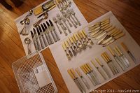 Full view of all cutlery pieces neatly laid out on two white cloths, including beige-handled silverplate knives and forks, stainless steel knives, forks, spoons, and associated white wire basket.