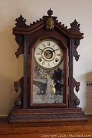 Front view of gingerbread clock showing overall wooden case, clock face, and Statue of Liberty etched glass door.