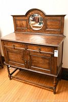 Front view of oak server showing drawers, cupboard doors, and oval mirror on decorative back panel