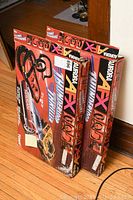Two boxed Aurora AFX Thunderloop Thriller race car track sets standing on a wooden floor, showing colorful graphics and box visual condition.