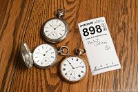 Three pocket watches and lot tag on wood surface