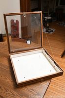 Open display case showing glass top, wooden frame, and white base with hole marks