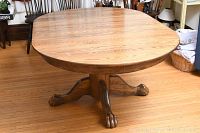Full front view of the wood pedestal dining table showing the tabletop and two extension leaves.