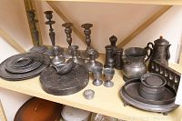 Wide shot of antique pewter items on shelf including candlesticks, ladle, plates, teapot, pitcher, and condiment holders