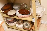 Overview of shelf showing brown and white casserole dishes, floral Corning Ware covered casserole, rectangular and oval bakeware dishes, and glass measuring cup.
