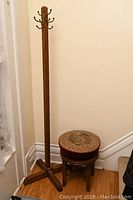 Full view of oak hall tree with metal hooks and wood piano stool with needlepoint seat beside it