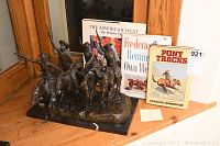 Multi‐item shot showing bronze‐color sculpture on marble base with three books behind